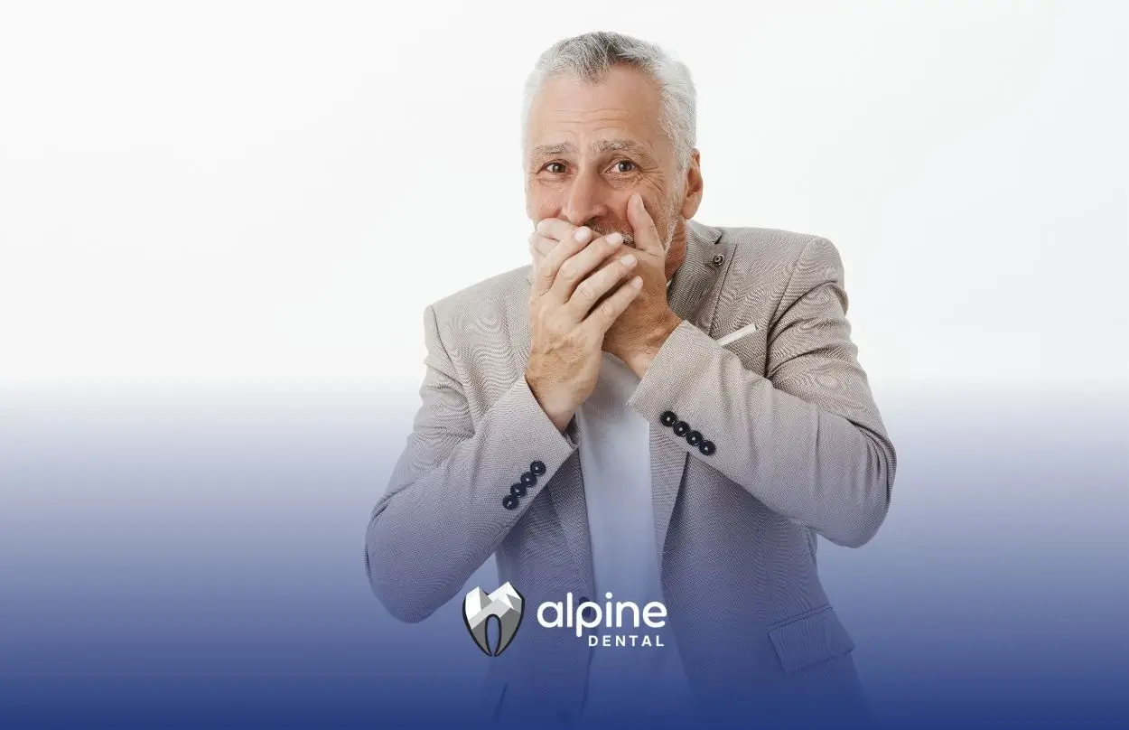 Older adult man covering his mouth to represent concerns about chronic bad breath & oral health issues affecting confidence.