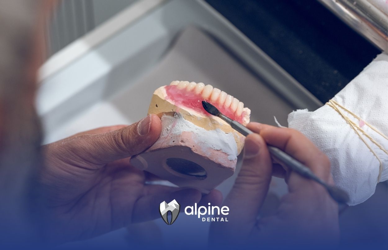 Dental professional repairing a denture model by applying material to artificial teeth during a close-up procedure.