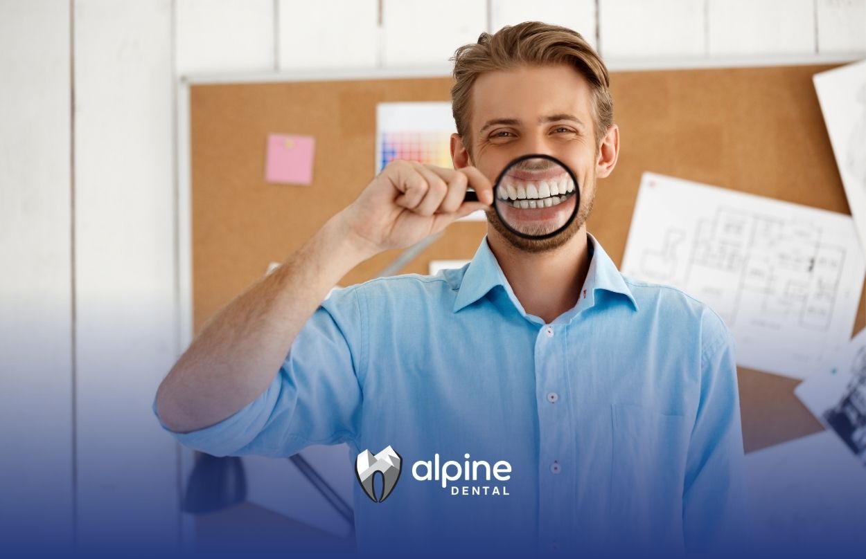 Man examining his teeth with a magnifying glass to highlight dental concerns and signs that a tooth crown may be needed.