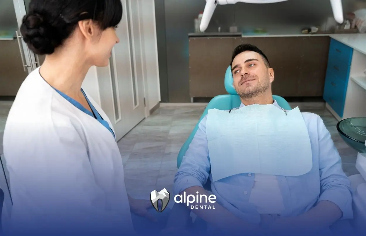 Dentist speaking with a relaxed patient seated in a dental chair, wearing a protective bib during a dental consultation.