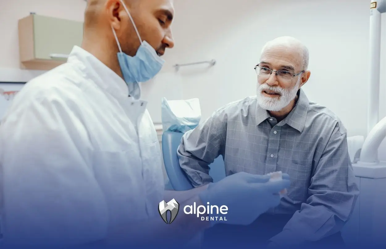 A dentist wearing gloves explains a dental bridge to an older patient during a consultation in a modern dental clinic.