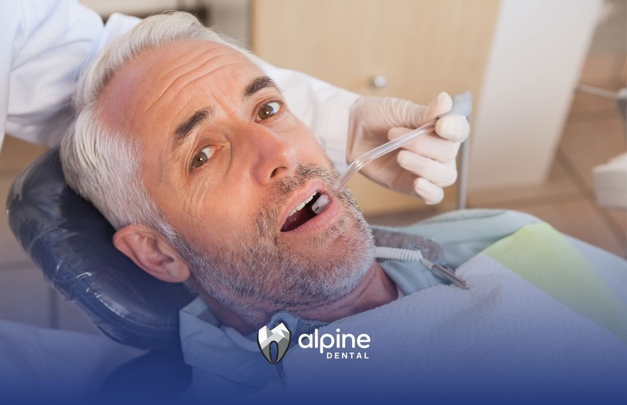 Older adult receiving dental care while lying in a dental chair with a professional examining his teeth and gums.