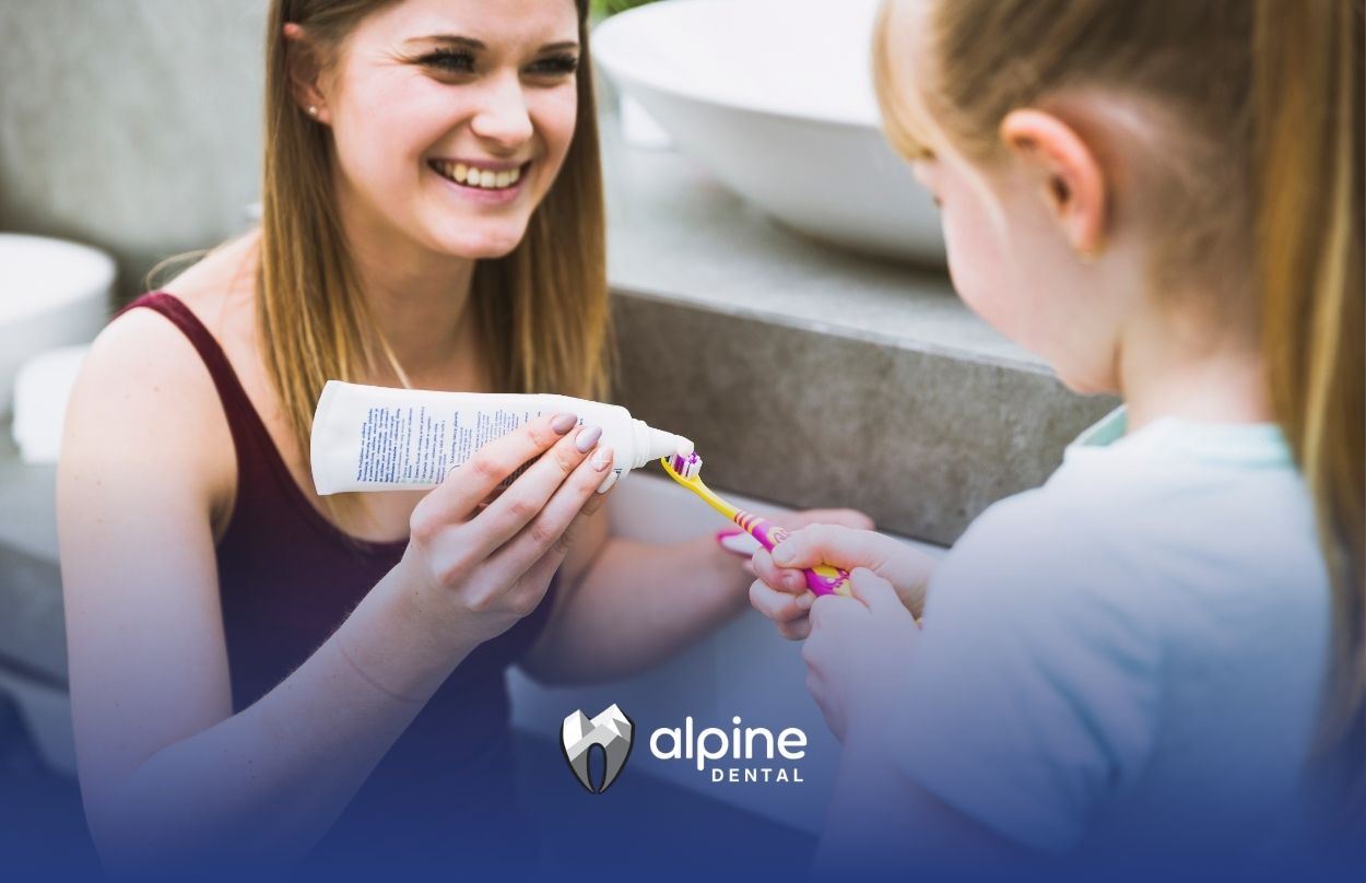 Child receiving fluoride varnish preparation as a parent applies toothpaste to a toothbrush during a dental care routine.